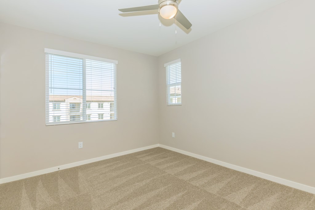 an empty living room with a ceiling fan and two windows