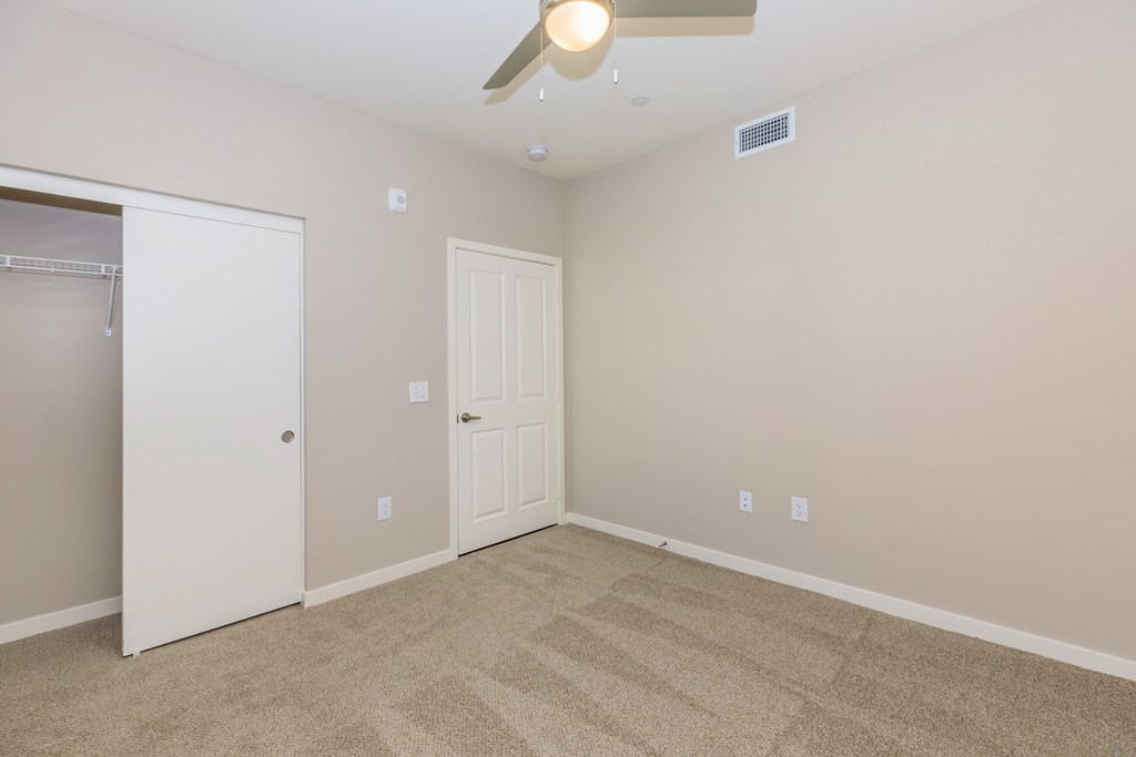 a empty bedroom with a ceiling fan and a closet