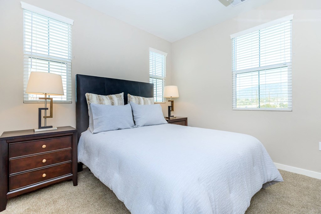 a bedroom with a bed and two night stands and two windows