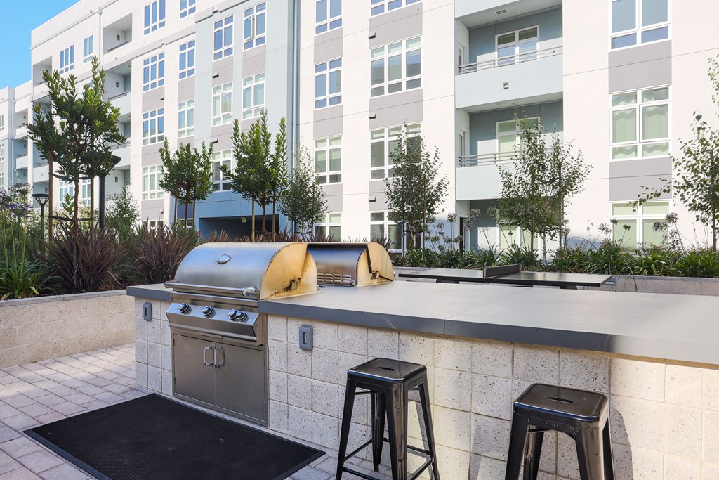 an outdoor kitchen with a grill and stools in front of an apartment building
