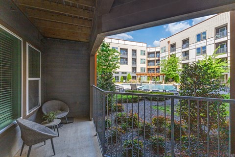 A balcony with a chair and a table overlooks a pool and buildings.