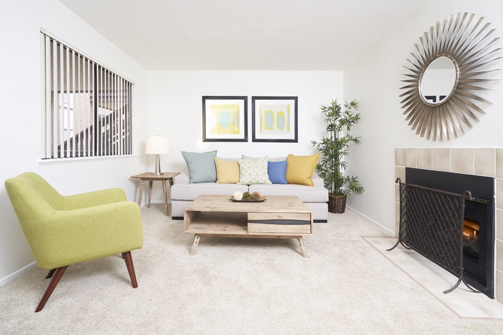 Apartments In Thousand Oaks, CA, For Rent - The Knolls - Living Room With Carpet Flooring, Couch with Throw Pillows, Coffee Table, Side Table with Lamp, Armchair, Fireplace, And Window with Blinds