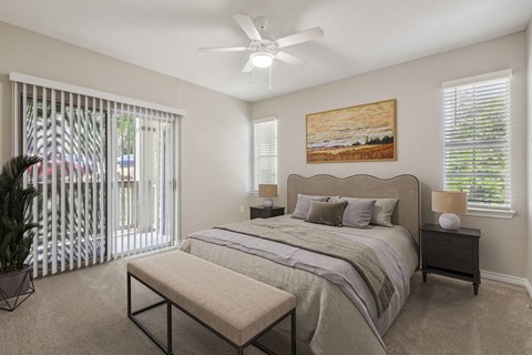 Pet-Friendly Apartments in North Austin, TX - Museo Channings Mark - Bedroom With Carpet Flooring, Queen Bed, Bed Bench, Nightstands With Lamps, Ceiling Fan, And Sliding Glass Doors.