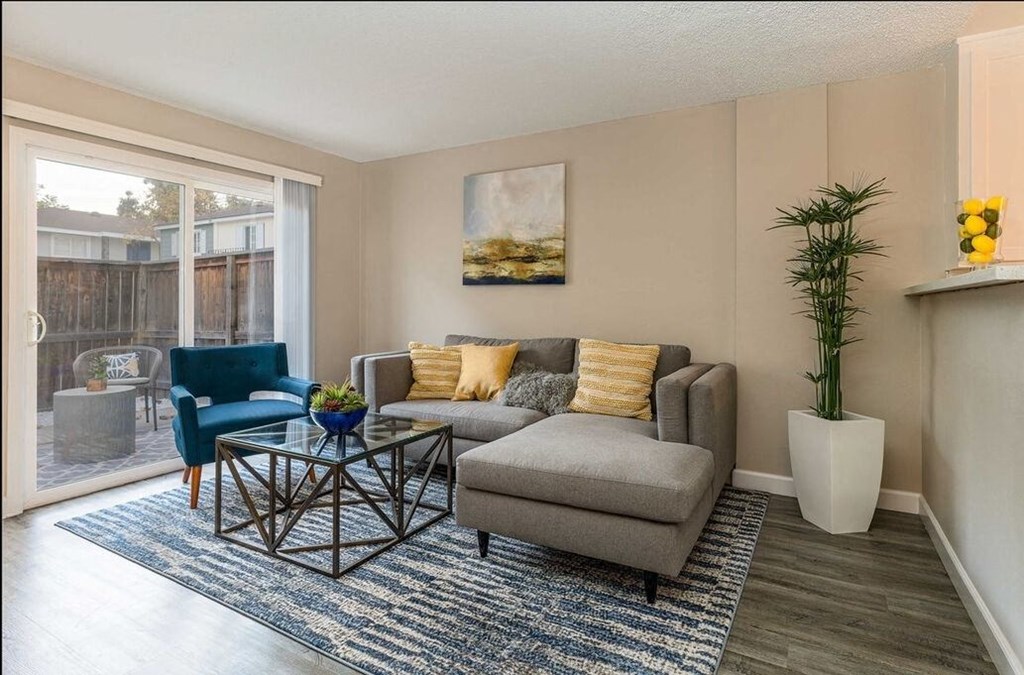 A living room with a grey couch, a blue chair, a coffee table, and a painting on the wall at Nola 624 Apartments, West Covina, California