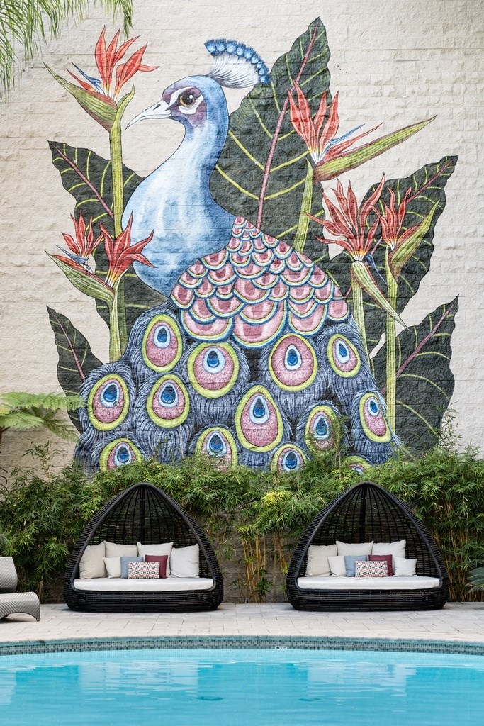 a mural of a peacock on the side of a building with lounge seating by the pool