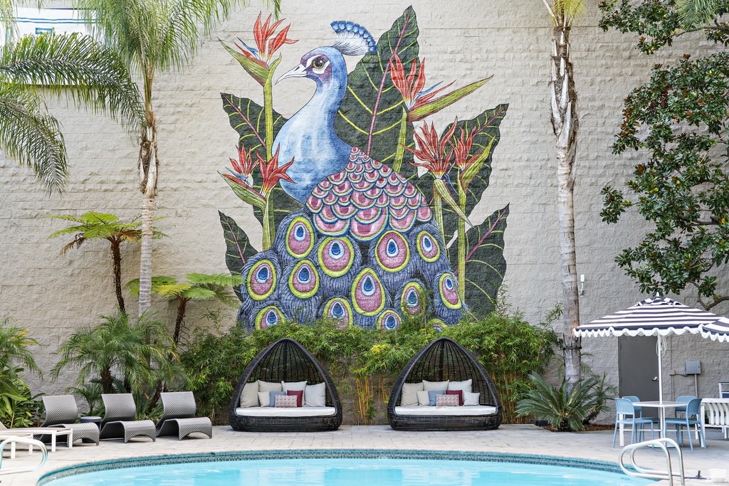 a mural of a peacock on the side of a building with lounge seating by the pool