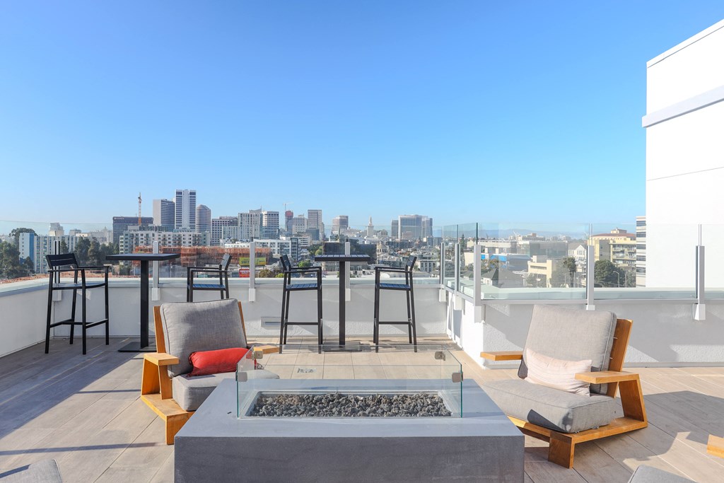 a rooftop terrace with chairs and a fire pit and a city in the background