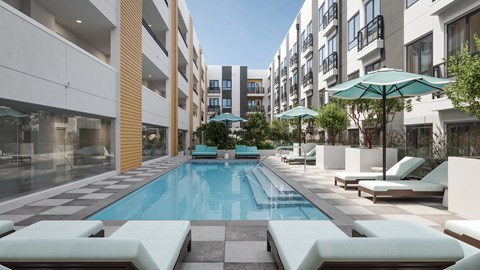 A swimming pool surrounded by lounge chairs and umbrellas in a modern building.