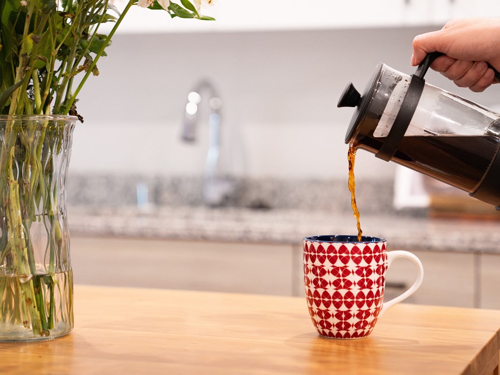 a person pouring coffee from a coffee pot into a red and white mug