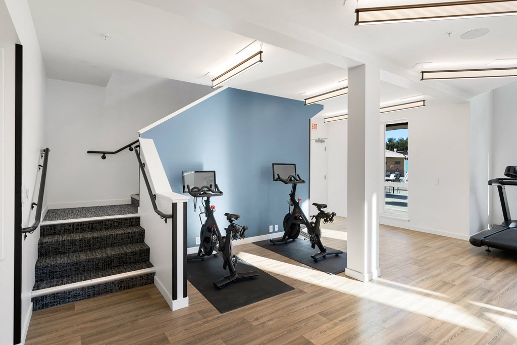 a gym with exercise equipment and stairs in a home with white walls and wood floors