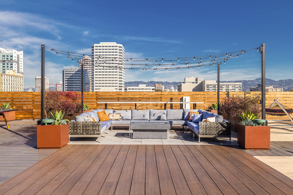 Luxury Studio Apartments Downtown Oakland CA - Alice House - Rooftop Terrace with Wooden Fencing, Plant Boxes, Seating Area with Couches and String Lights Overhead, and Beautiful Cityscape Views