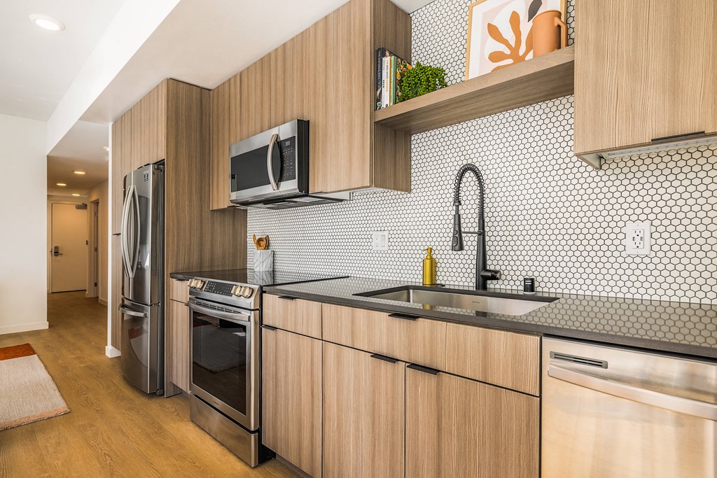 Two Bedroom Luxury Apartments in Downtown Oakland CA - Alice House - Modern Kitchen with Stainless Steel Appliances, Hexagonal Tile Backsplash, Wood-Style Cabinetry, Storage Shelving, and Hardwood Style Flooring