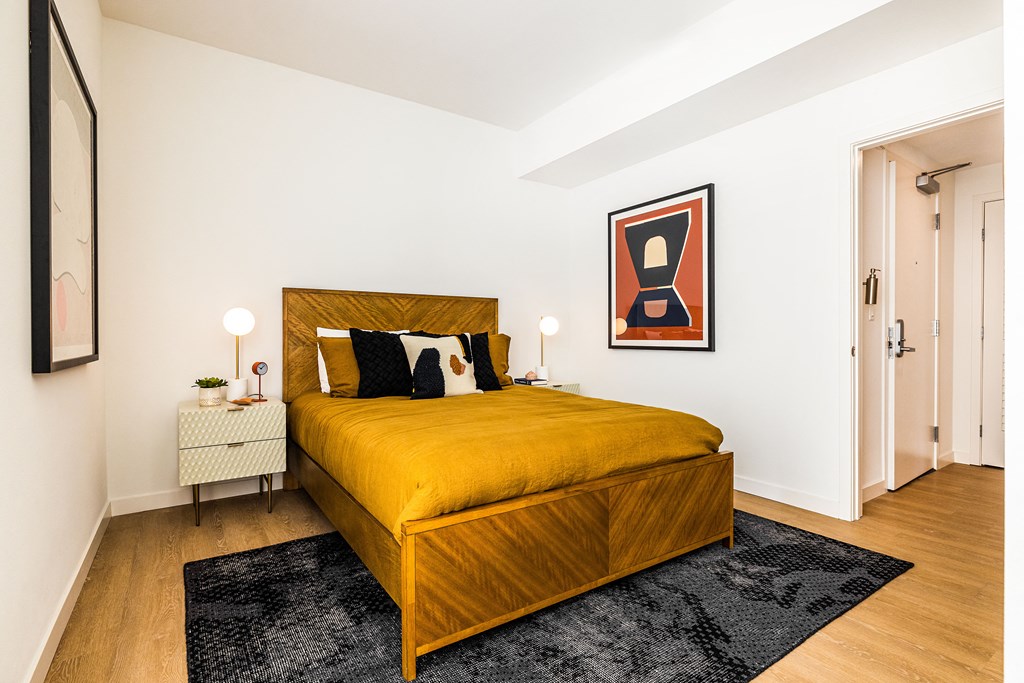 One Bedroom Luxury Apartments in Downtown Oakland CA - Alice House - Furnished Bedroom with a Wooden Bed, Hardwood Style Flooring, Rug, Two Cream Nightstands with Drawers and Lamps, and White Walls