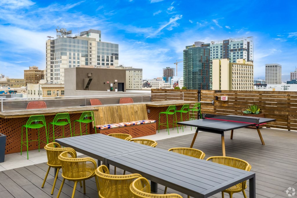 a rooftop patio with tables and chairs and a city in the background
