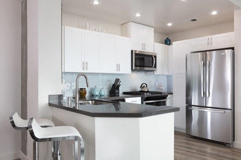 Kitchen with stainless steel appliances and bar seating at Aqua Via Apartments, Oakland, CA