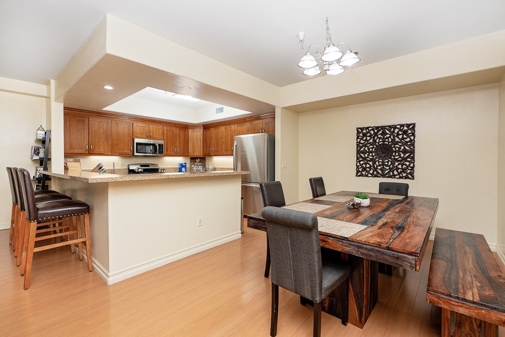 a dining area with a wooden table and chairs and a kitchen in the background