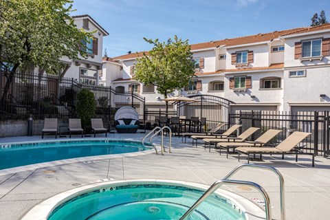 A pool with a ladder and chairs in front of apartment buildings.