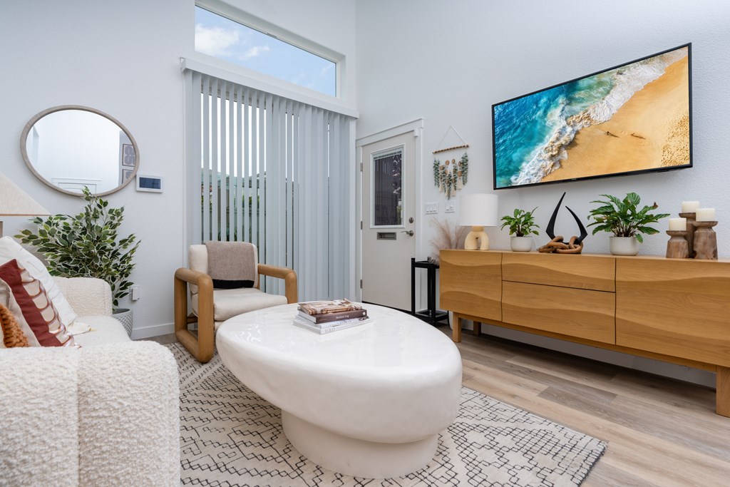A modern living room with a white sofa, a round mirror, and a flat-screen TV mounted on the wall.