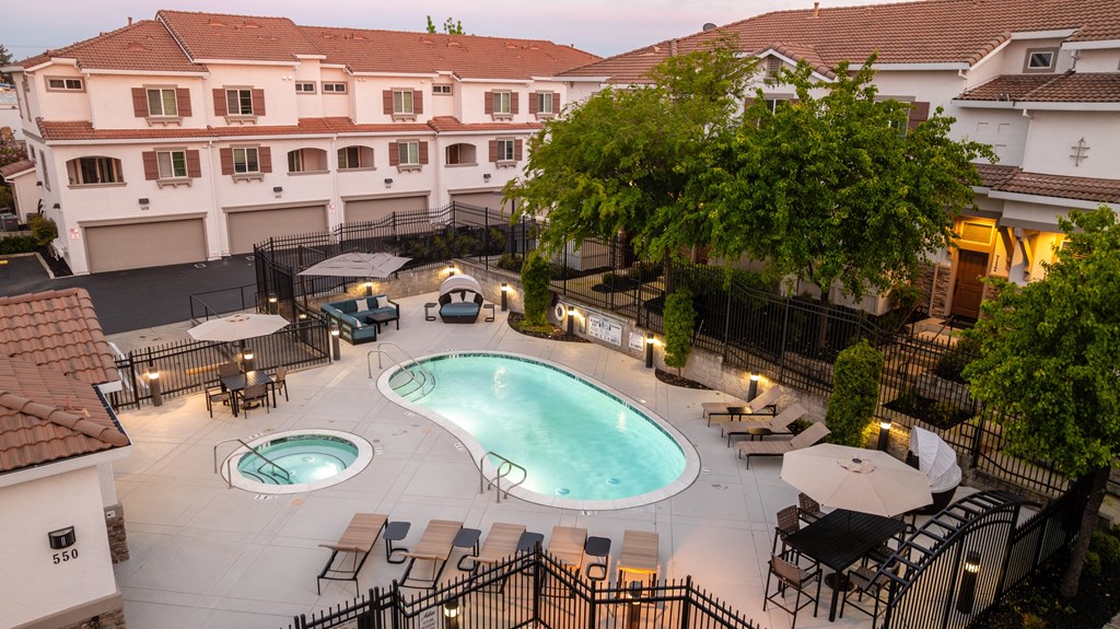 A large outdoor swimming pool surrounded by a black fence and patio furniture.