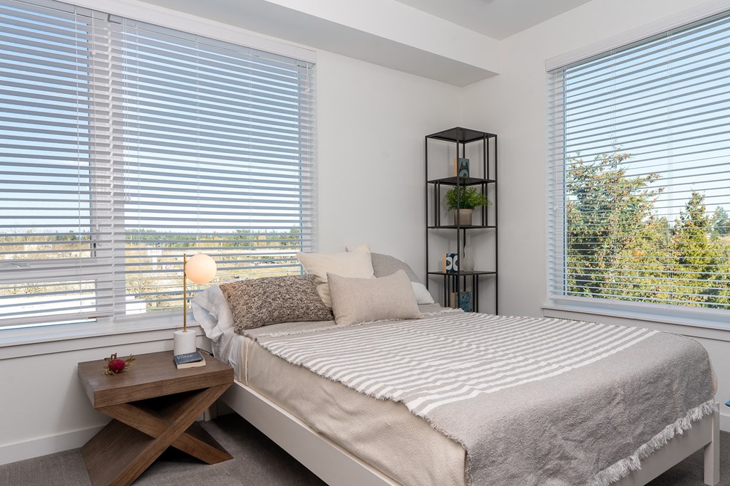 a bedroom with two large windows and a bed with a blanket and pillows