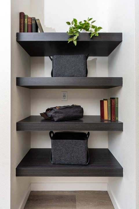 A shelf with three shelves has a plant on top, a bag, and books.