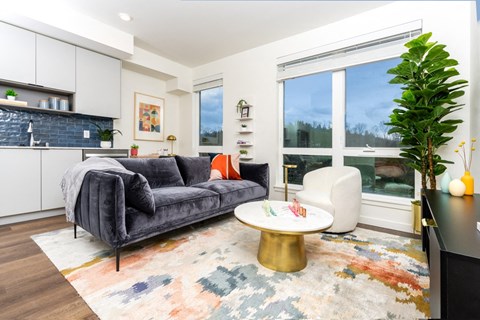 A living room with a grey couch, a coffee table, and a large window.