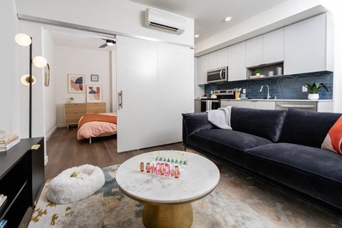 A modern living room with a black couch and a coffee table with a "Happy Birthday" cake on it.