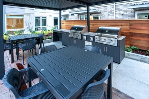A black table and chairs are set up on a patio with a grill.