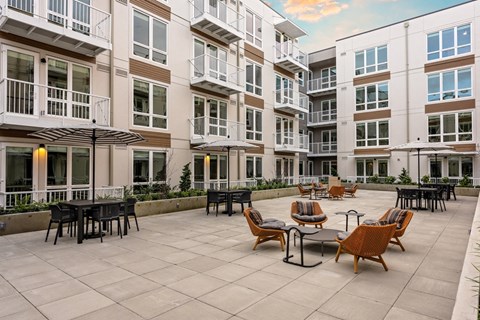 A patio with chairs and tables is surrounded by apartment buildings.
