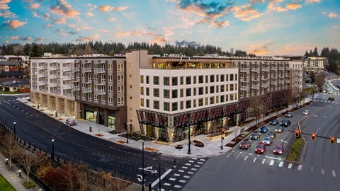A large apartment complex is situated on a street corner with cars parked along the curb.