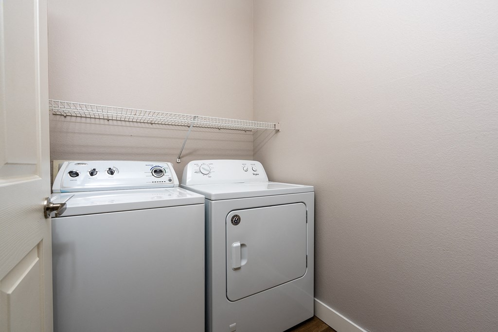 a washer and dryer in the corner of a room with a shelf above