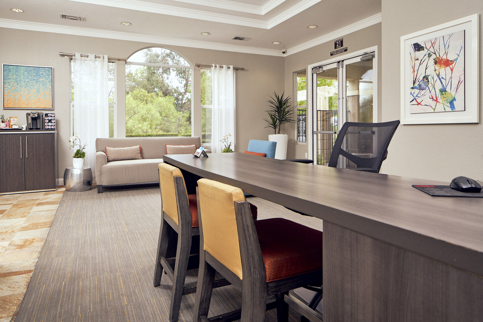 Apartments In Escondido, CA - Leasing Office With Office Desk, Coffee Station, Sliding Glass Door, Large Window, And Waiting Area