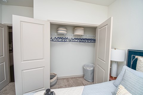 A small bedroom with a bed, a nightstand with a lamp, a trash can, and a closet with shelves.