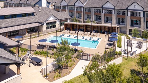 A large swimming pool surrounded by a grassy area and buildings in the background.
