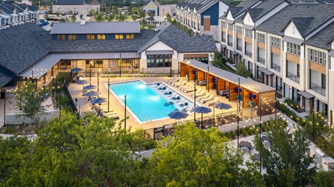 A large swimming pool surrounded by lounge chairs and umbrellas is the centerpiece of a resort-style outdoor area.