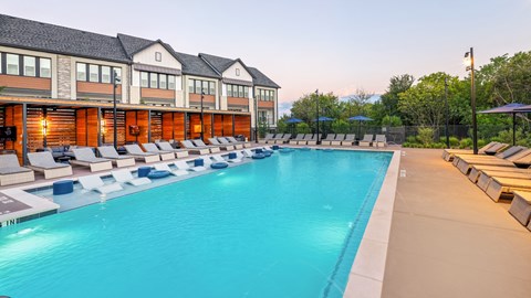A large swimming pool with lounge chairs and umbrellas in front of a building.