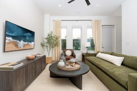 A living room with a green couch, a coffee table, and a painting of a beach scene on the wall.