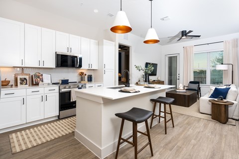 A kitchen with white cabinets and a white island with a bar stool in front of it.