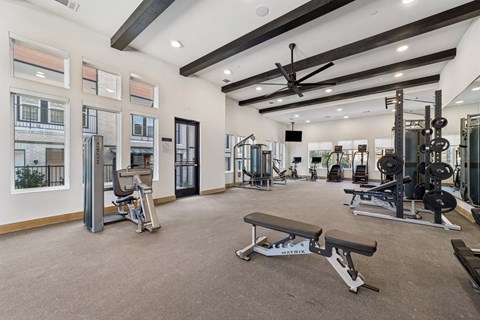 A spacious gym with a variety of equipment and a view of a building outside the windows.