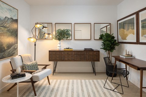A living room with a chair, a table, a plant, and a painting on the wall.