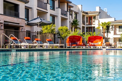 A pool with chairs and umbrellas in front of a building.