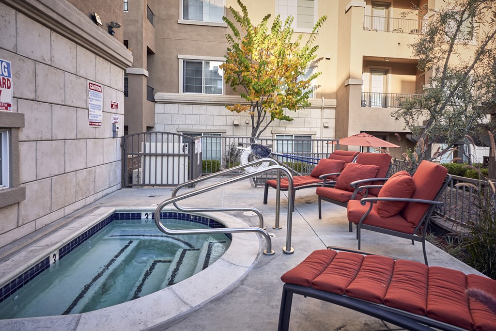 Apartments in San Jose CA - Aviara - Jacuzzi with Tiled Wall, Silver Rails, Red Lounge Seats, and Surrounding Trees and Gate