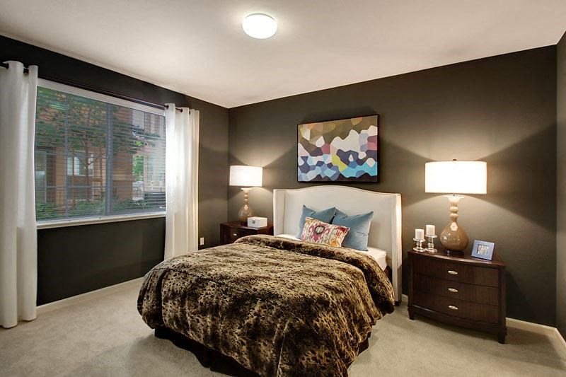 Two Bedroom Apartments in San Jose CA - Aviara - Furnished Bedroom with Bed, Black Walls, Large Window with Curtains and Blinds, Light-Colored Wall-to-Wall Carpeted Floors, Dark Wooden Nightstands with Lamps, Framed Art, and Overhead Lighting