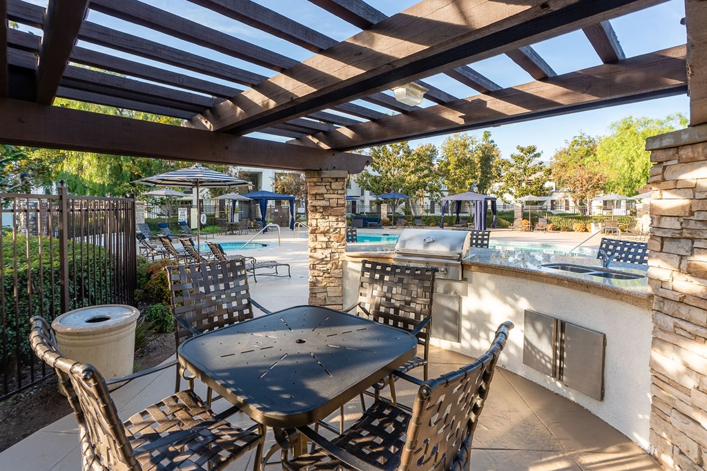 Rancho Cucamonga Apartments for Rent - Barrington Place - Poolside BBQ Area Under a Pergola, with Grill Station, Double-Sink, Table, and Chairs