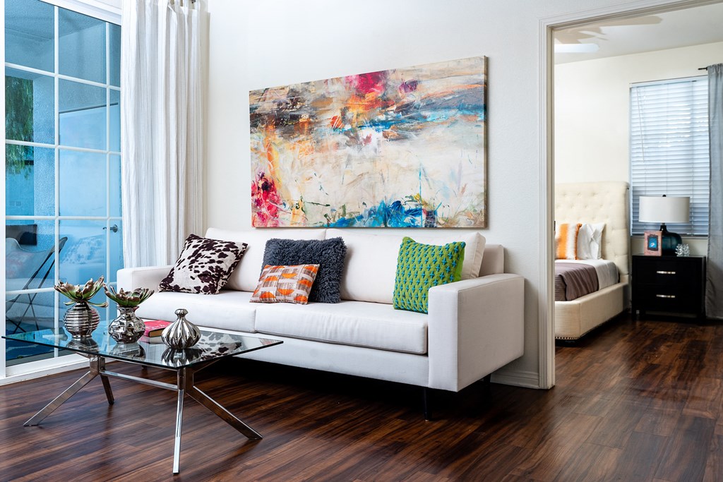 Two Bedroom apartments in Rancho Cucamonga CA - Barrington Place - Living Room with Wood-Style Flooring, White Couch, Glass-Top Coffee Table, Wall Art, and Large Window