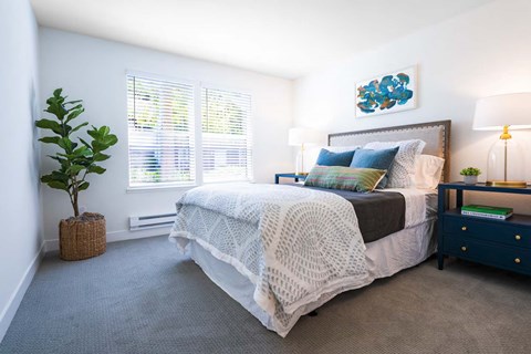 A bedroom with a bed, nightstand, and a plant.