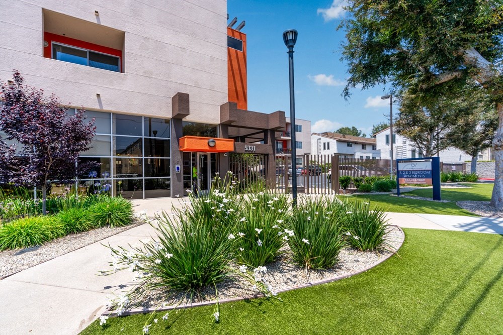 a sidewalk in front of a building with grass and flowers