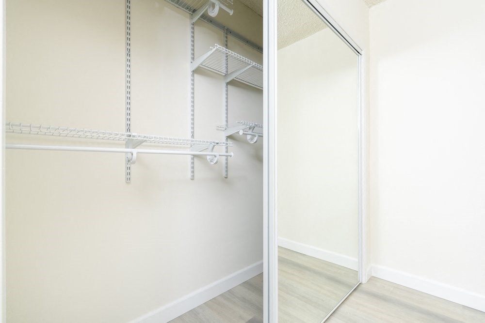 two views of a mirrored closet in a bedroom with white walls and wood floors