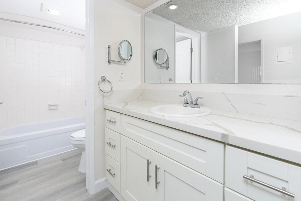 A white bathroom with a tub, sink, and mirror.