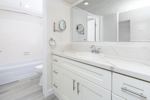A white bathroom with a tub, sink, and mirror.